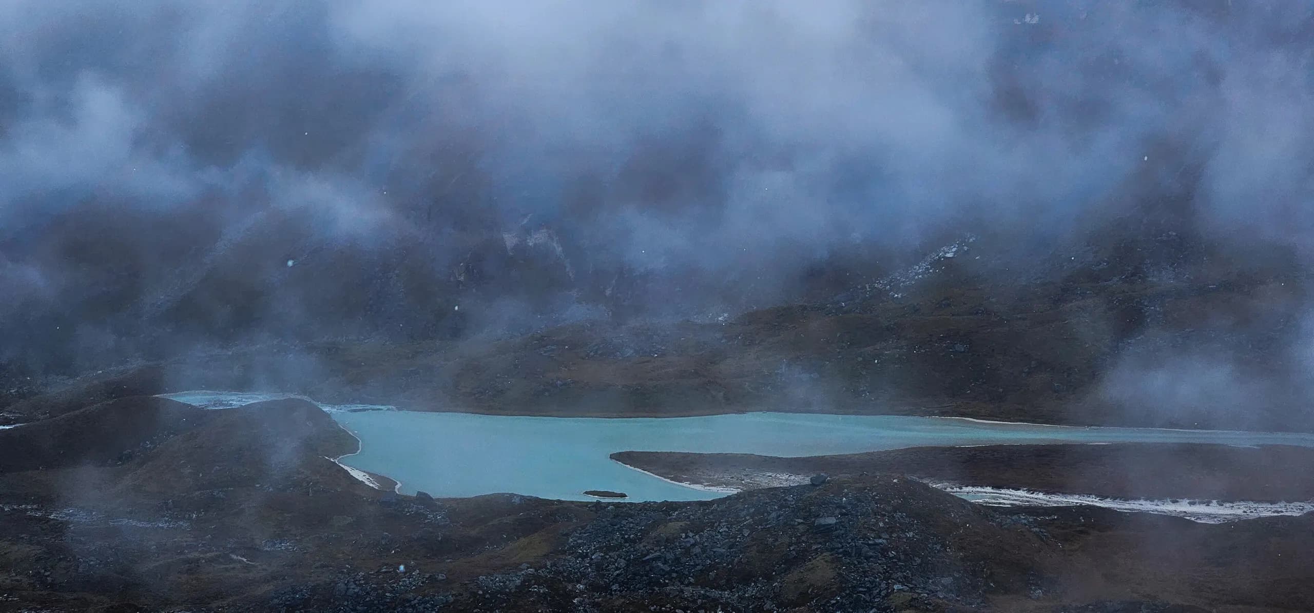 A turquoise glacial lake below Mera Peak shrouded in cold blue mist