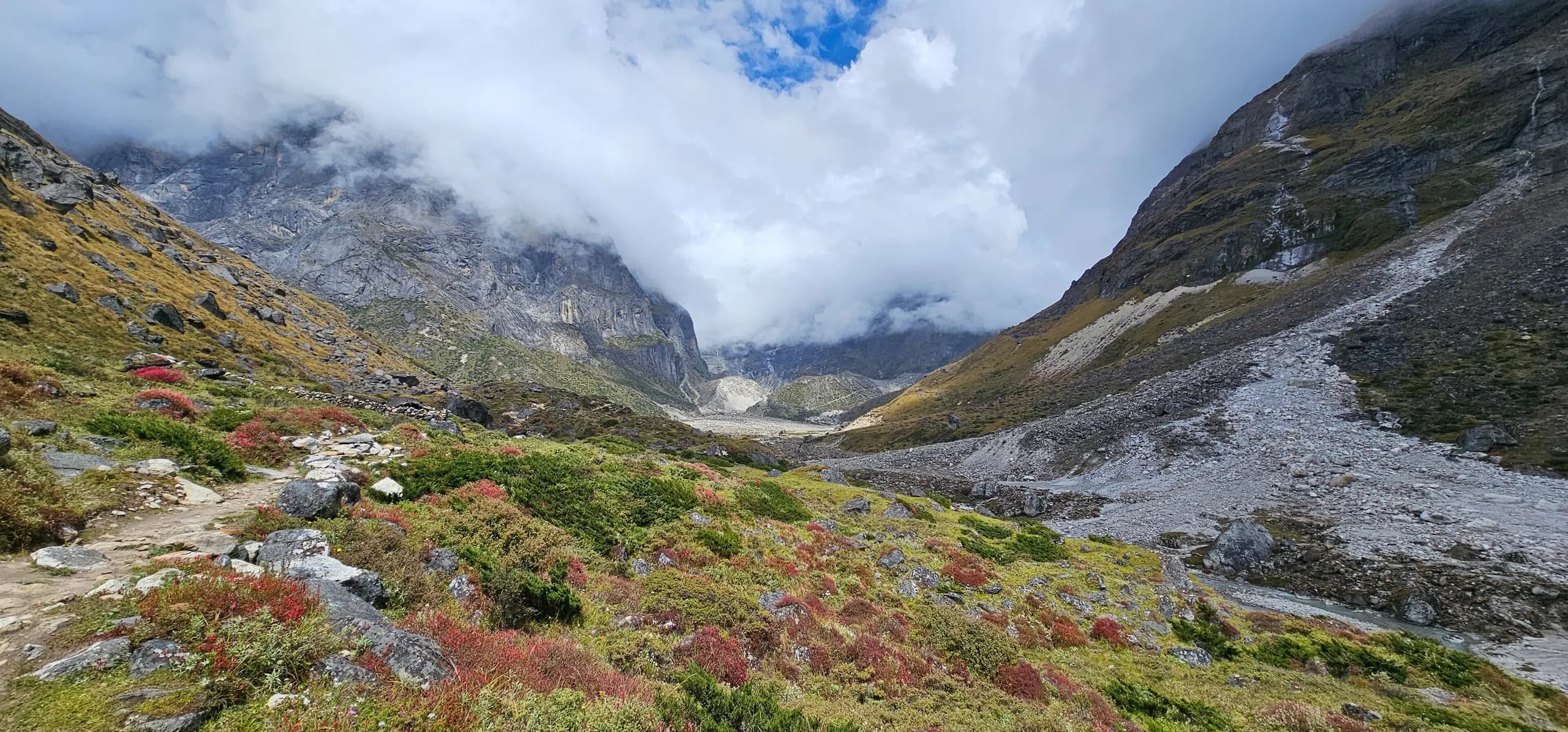 Trail through the Hinku Valley with alpine shrubs and moraine below cloud-wrapped peaks